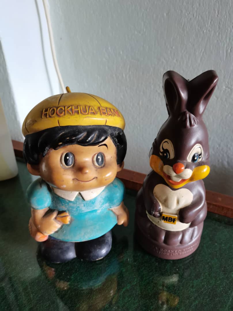 左邊的學童撲滿爲來自福華銀行(Hock Hua Bank)的贈品或紀念品,右邊的兔子撲滿則來自馬婆金融(MBf Finance Berhad)。兩者皆爲現已不存在的馬來西亞銀行/金融機構。